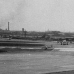 RW15R（A滑走路） からツインボナンザが離陸　あちら側にいる機体はJALのDC-6B？、全日空のDC-3貨物機も見える。1964年（昭和39年）頃。（森）